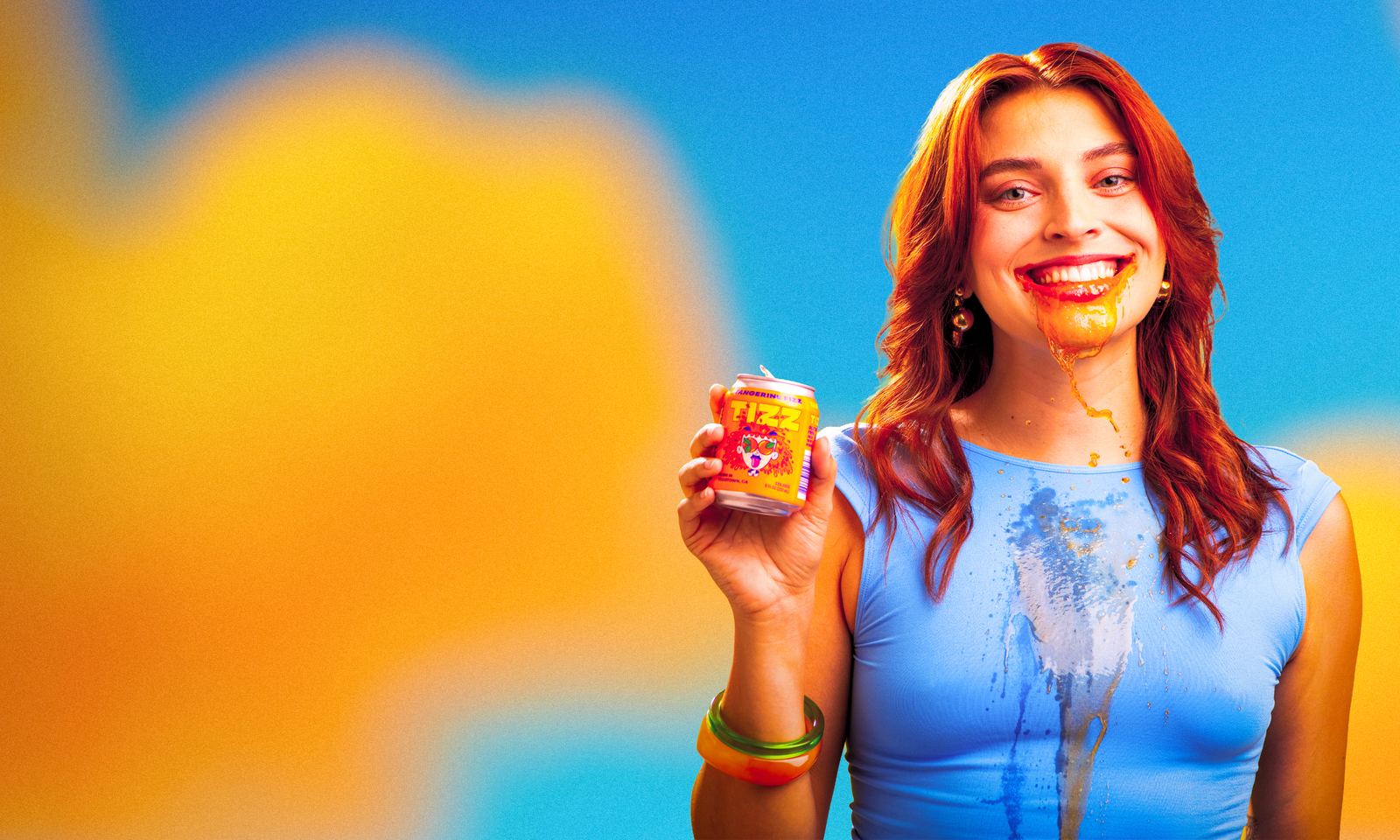 Smiling woman holding an 8oz can of TIZZ with tangerine soda dripping down her chin